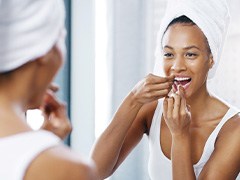 Woman smiling while flossing teeth in bathroom