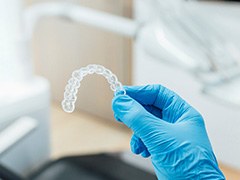 Dentist with blue glove holding clear aligner