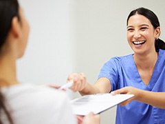 Smiling dental assistant handing patient forms