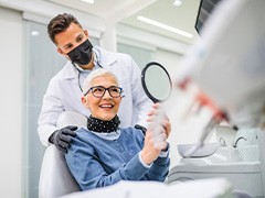 Woman with black glasses smiling at reflection in handheld mirror