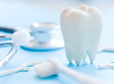 Model of a tooth and various dental tools on blue background