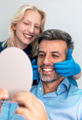 Dentist touching man’s face with blue-gloved hands as he smiles into mirror