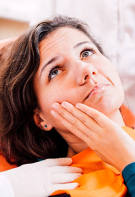 Woman in dental chair touching jaw with hand as two dentists touch her shoulders