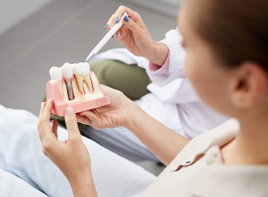 dentist showing a patient a model of a dental implant in the jaw 