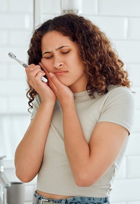 Woman holding a toothbrush and rubbing her jaw