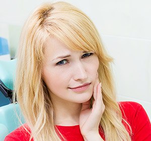 woman in red holding jaw in pain