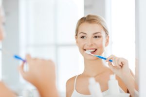 Woman brushing her teeth to prevent a dental emergency.