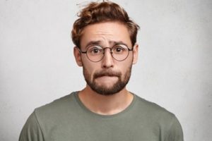 Man wearing a gray shirt and glasses biting his bottom lip with a worried look on his face