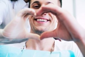 Man smiling and making half of a heart shape with his hand while a gloved hand makes the other half of the heart