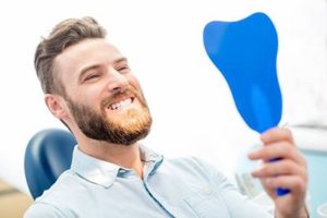 Man with healthy smile looking in dental mirror