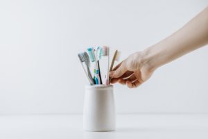 Hand reaching for one of several toothbrushes in an off-white holder