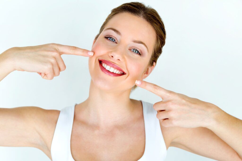 Woman in white tank top pointing to her smile