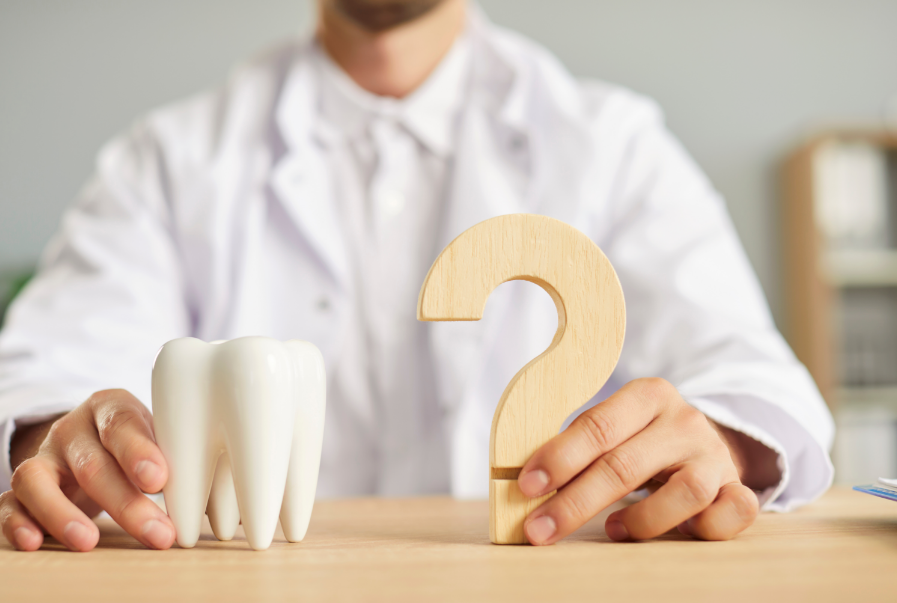 Photo of a dentist holding a model tooth and a question mark